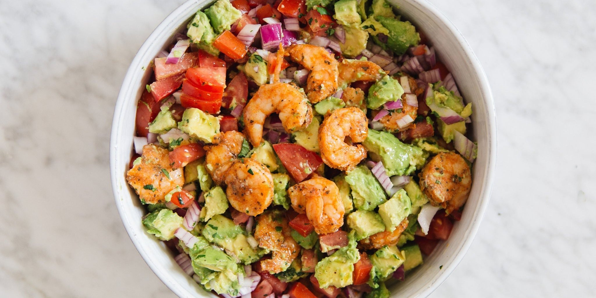 Prime Shrimp Signature Seasoned in white bowl with avocado, red peppers, and red onion. On marble counter. 